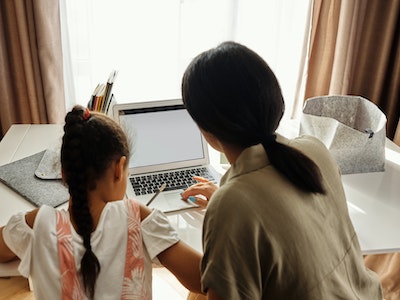 Behind shot of mum helping daughter with work on a desk. 