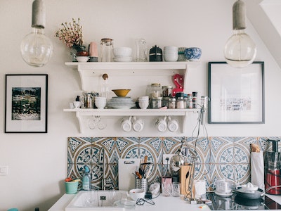 A busy kitchen/sink area with plenty of crockery, and framed pictures either side of a shelf.