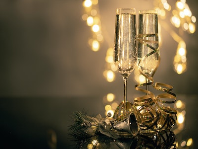 Two champagne flutes with gold decor and gold lighting out of focus in the background.